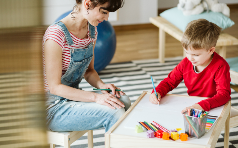 Woman sitting with young boy as he colors