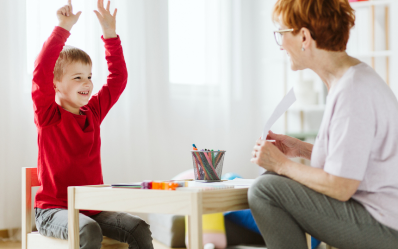 Woman sitting at kids table with young boy holding his hands in the air
